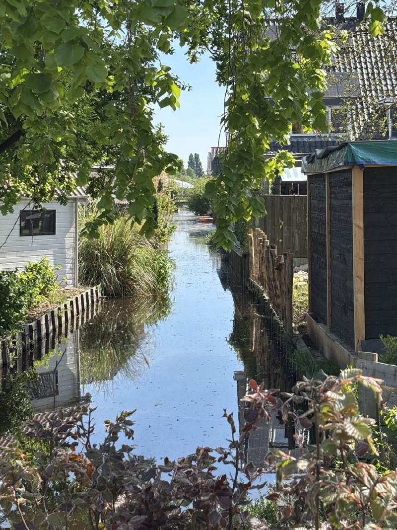 一條窄窄的水道穿過住家後院,遠處一座小橋,岸邊泊著一艘小船。